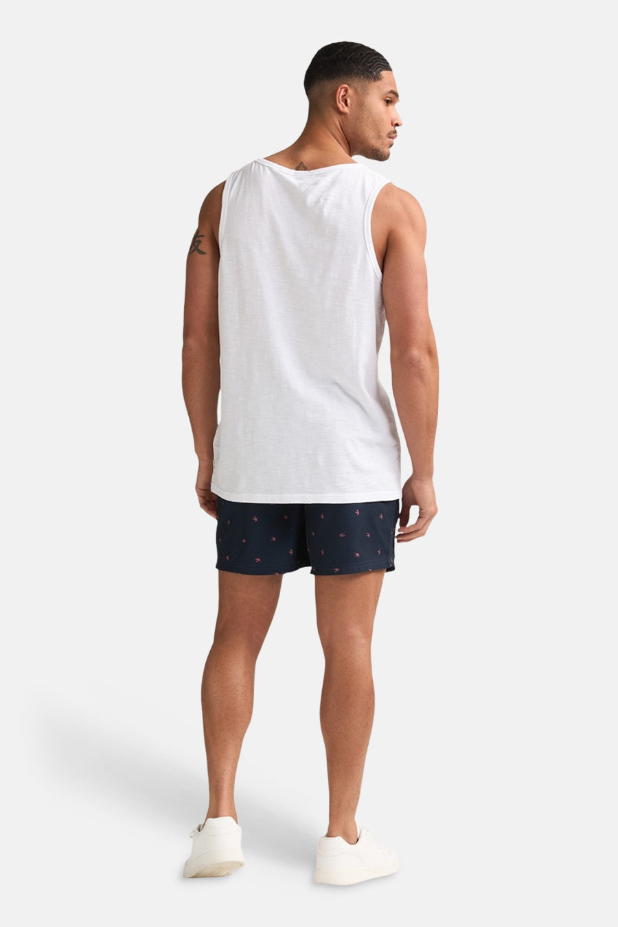 Witte singlet van Petrol Industries, van achteren gezien op een man met donkerblauwe shorts met vogelprint en witte sneakers.