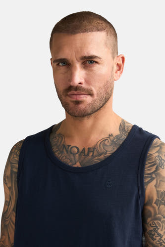 Débardeur bleu de Petrol Industries, porté par un homme avec des tatouages sur la poitrine et les bras.