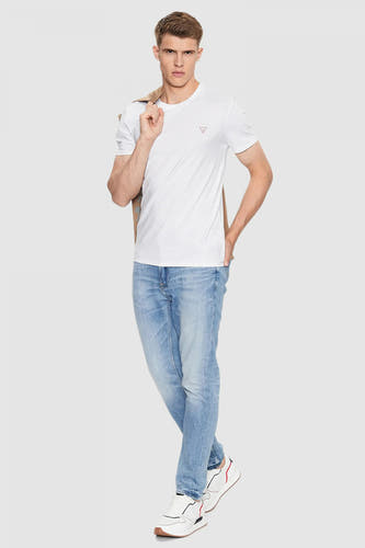 T-shirt blanc à manches courtes de Guess, avec un manteau sur l'épaule et des jeans légers et des baskets blanches.