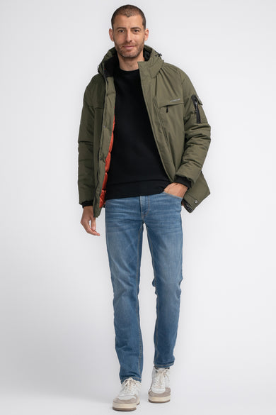 Veste de pluie khaki de Petrol Industries, portée avec un pull noir et des jeans bleus, en position debout.