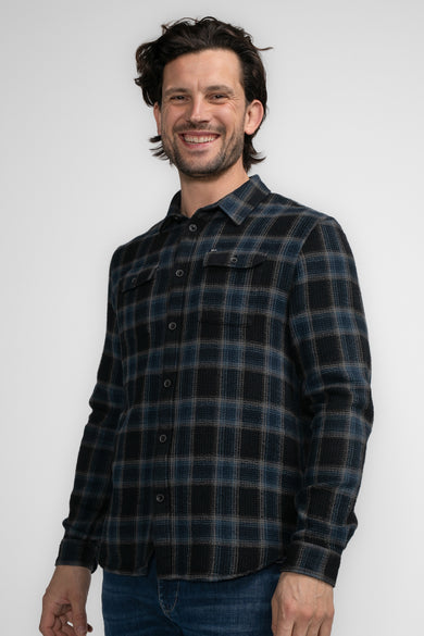 Chemise noire à manches longues de Petrol Industries, avec un motif de carreaux bleu et noir, portée avec un jean.