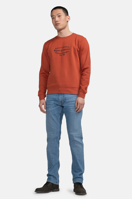 Pull-over rouge de Petrol Industries, avec un col rond, associé à des jeans et des chaussures sombres.