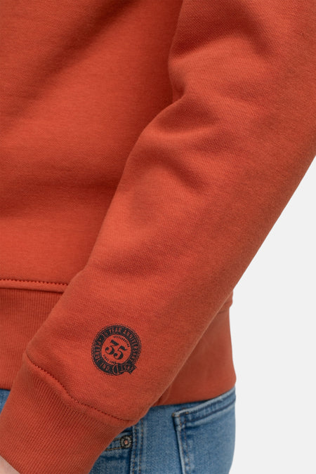 Gilet rouge de Petrol Industries, avec des manches longues et une badge ronde de 55 ans sur la manche.