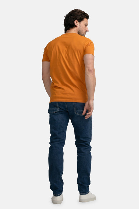 Oranje T-shirt met korte mouwen van Petrol Industries, gezien van achteren, gecombineerd met donkere jeans en witte sneakers.
