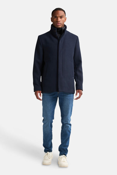 Manteau long bleu de Petrol Industries® avec un col montant, des jeans et des baskets.