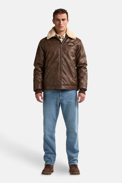 Manteau court brun de Petrol Industries avec un col en fourrure synthétique, porté sur une chemise et des jeans bleus.