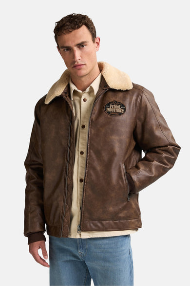 Veste courte brune de Petrol Industries, avec col en fourrure et poches à fermeture éclair, portée sur une chemise beige et des jeans bleus.