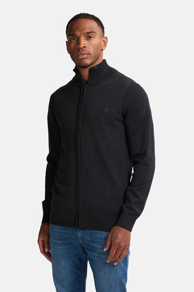 Gilet noir de Petrol Industries avec une fermeture à glissière et un col côtelé, porté avec un jean bleu.