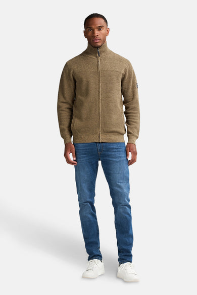 Gilet beige de Petrol Industries, avec une fermeture éclair et porté avec un jean bleu et des baskets blanches.
