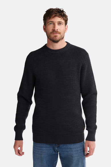 Pull noir à col rond de Petrol Industries®, avec un fin motif rayé et des bordures côtelées, porté avec un jean bleu.