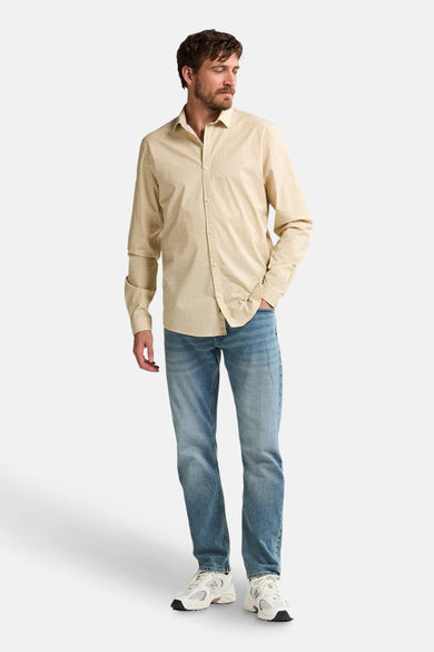 Chemise beige à longues manches de Petrol Industries, portée avec des jeans bleus et des baskets blanches.