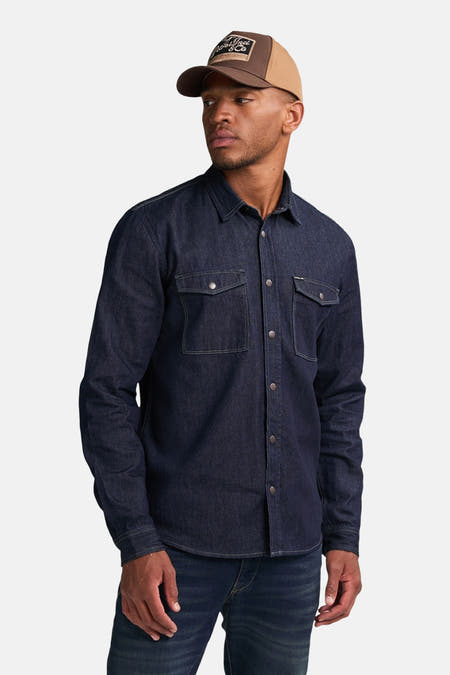 Chemise en denim bleu marine à longues manches de Petrol Industries® avec poches poitrine et fermeture à boutons, associée à des jeans et un casque.