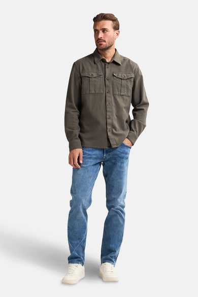 Chemise verte à manches longues de Petrol Industries, avec des poches po po et portée sur un jean bleu et des baskets crème.