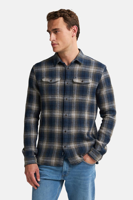 Chemise bleue à manches longues de Petrol Industries, avec un motif à carreaux et des poches po poitrine, portée avec un jeans bleu.