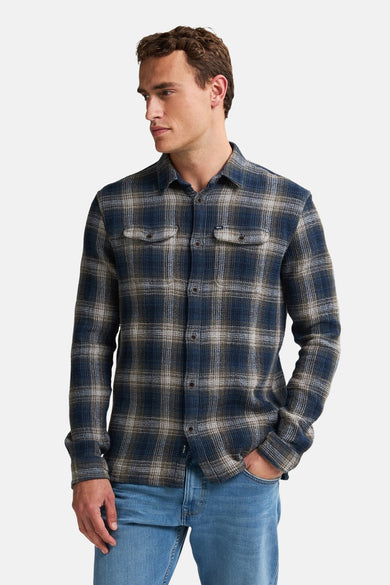 Chemise bleue à manches longues de Petrol Industries, avec un motif à carreaux et des poches po poitrine, portée avec un jeans bleu.
