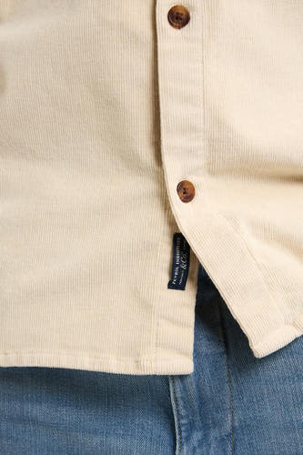 Chemise beige à longues manches de Petrol Industries, texture corduroy et col boutonné, portée avec un jean bleu.