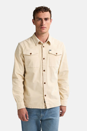 Chemise beige à manches longues de Petrol Industries, avec des boutons bruns et deux poches po poitrine, portée avec un jean bleu.
