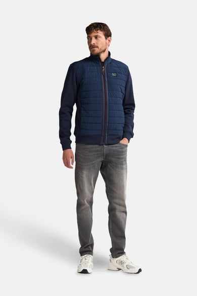 Manteau court bleu de Petrol Industries, avec fermeture éclair et jeans gris et baskets blanches.