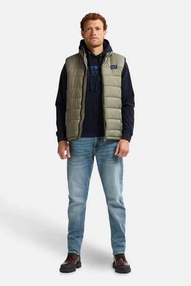 Gilet bodywarmer de Petrol Industries, porté sur un hoodie bleu marine et des jeans bleus, avec des baskets marrons.