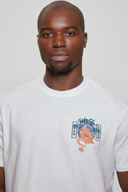 Wit T-shirt met korte mouwen van Guess, met een oranje draak en 'Guess West Coast' opdruk op de borst, gedragen door een man.