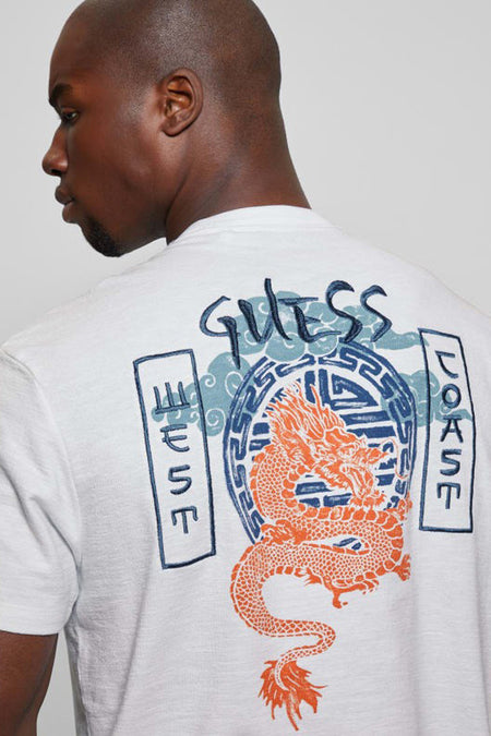 T-shirt blanc à manches courtes Guess avec un dragon orange et l'inscription 'Guess West Coast' dans le dos.