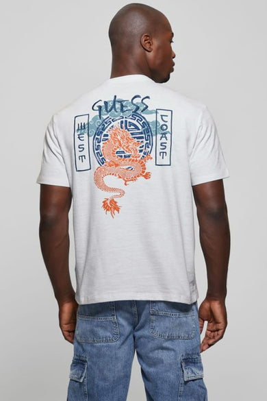 T-shirt blanc à manches courtes Guess, avec un dragon orange et l'inscription 'Guess West Coast' sur la poitrine, porté par un homme.
