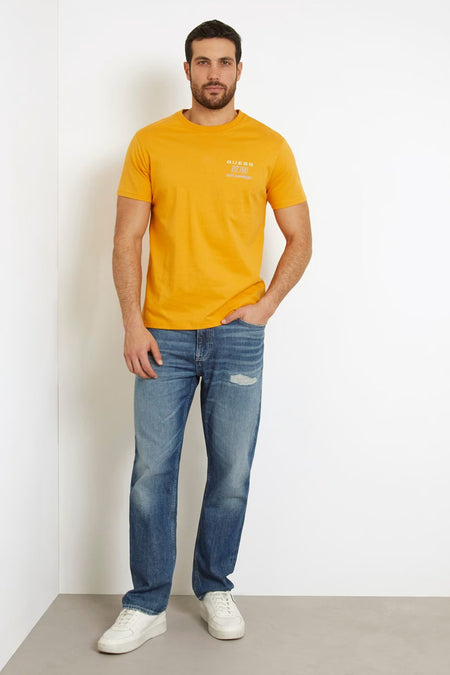 T-shirt orange à manches courtes de Guess, porté avec des jeans bleus et des baskets blanches.