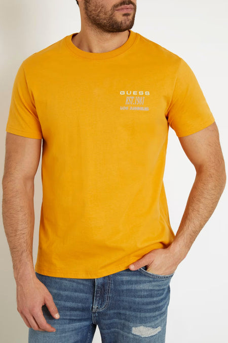 T-shirt orange de Guess à manches courtes, imprimé sur la poitrine et porté avec un jean.