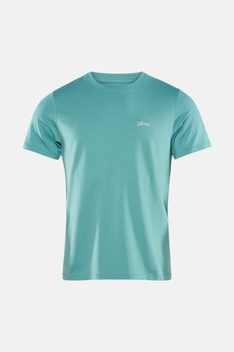 T-shirt vert à manches courtes Guess®, avec petit imprimé texte sur la poitrine, combiné avec un jean foncé et des baskets beiges.
