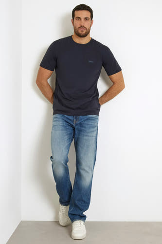 T-shirt bleu à manches courtes de Guess, avec jean et baskets blanches.
