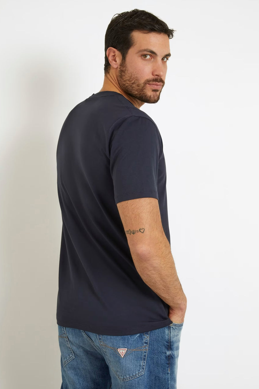 Blauw T-shirt met korte mouwen van Guess, zichtbaar is een tattoo op de arm en de jeans.
