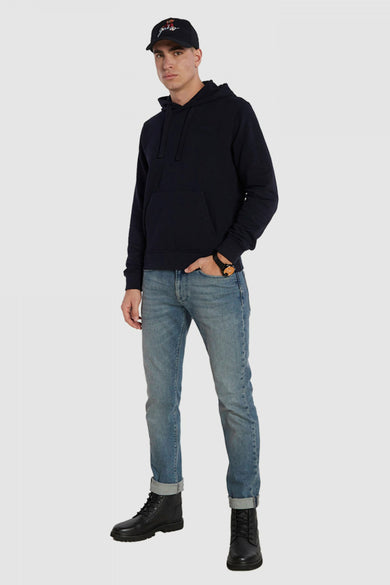 Pull-over noir avec capuche de Guess, associé à des jeans, des bottes noires et un chapeau.
