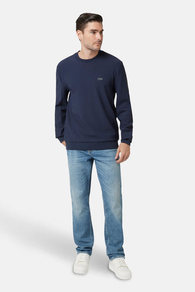 Pull-over bleu de Guess, avec des manches longues et un col rond, associé à des jeans et des baskets blanches.