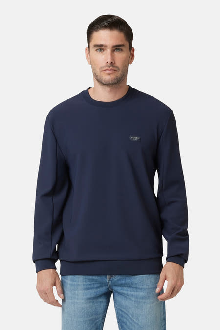 Pull-over bleu de Guess, avec des manches longues et porté avec un jean.