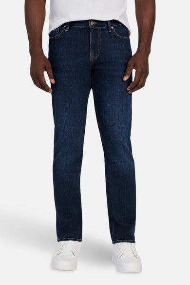 Jean slim de denim bleu foncé de Guess, porté avec un T-shirt blanc et des baskets blanches.