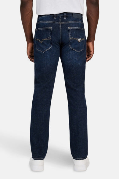 Jean slim de denim bleu marine de Guess, avec des poches arrière visibles et des baskets blanches.