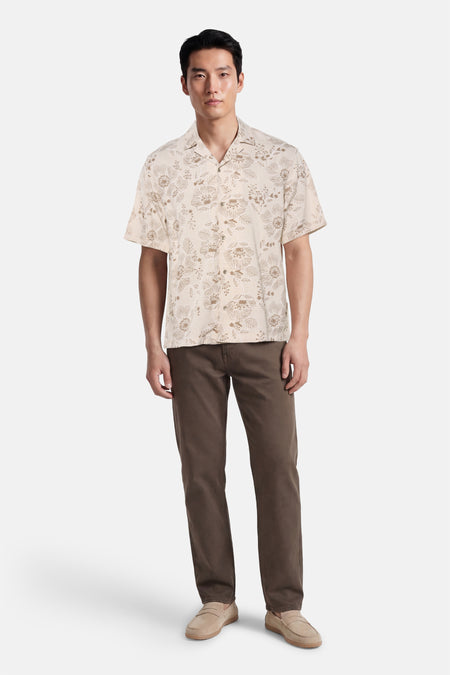 Chemise beige à manches courtes de Guess®, avec un motif floral et assortie à un pantalon et des chaussures marron.