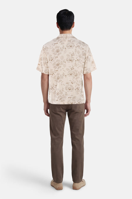 Beige hemd met korte mouwen van Guess®, met een bloemmotief en gecombineerd met bruine broek en schoenen.
