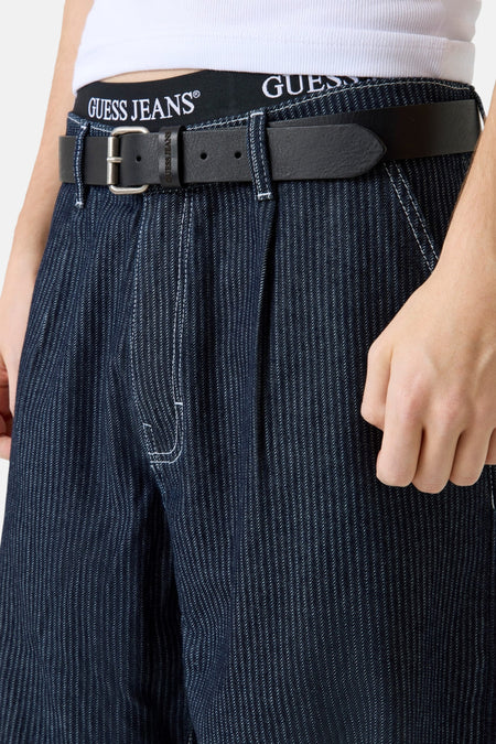 Jean large de denim bleu marine de Guess, avec des surpiqures blanches et une ceinture noire.