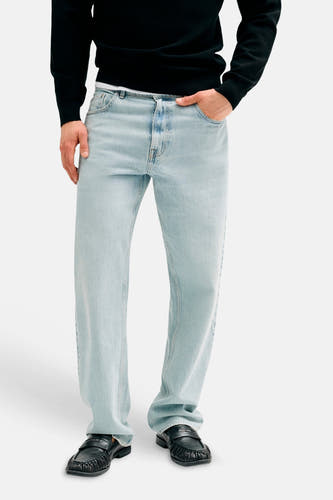 Jean droite bleu clair de Guess, porté par un mannequin avec un pull noir et des mocassins noirs.