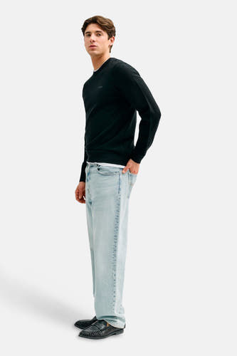 Jean droit bleu clair de Guess, porté par un homme de profil avec un pull noir et des mocassins.