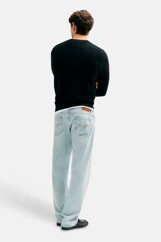 Jean coupe droite bleu clair en denim de Guess, avec un patch en cuir marron et des surpiqûres emblématiques sur les poches arrière.