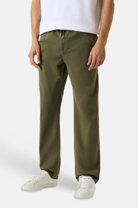 Pantalon vert Guess avec cordon de serrage à la taille, porté avec un t-shirt blanc et des baskets blanches.