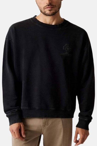 Pull-over noir avec col rond de Guess, avec petit logo sur la poitrine, porté avec un pantalon kaki.