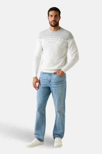 Sweat-shirt gris avec col rond de Guess, avec un logo sur la partie avant, associé à des jeans bleus et des baskets blanches.