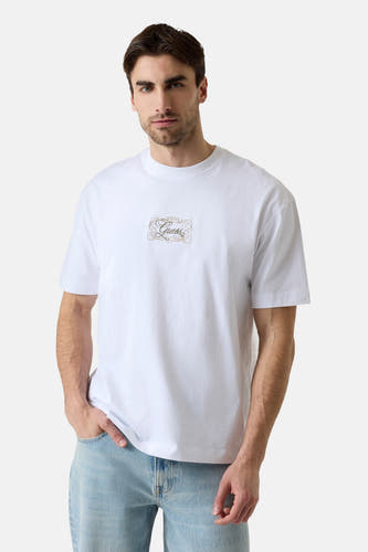 Witte korte mouwen T-shirt van Guess® met goudkleurig logo op borst, gedragen door model in lichte jeans, front view