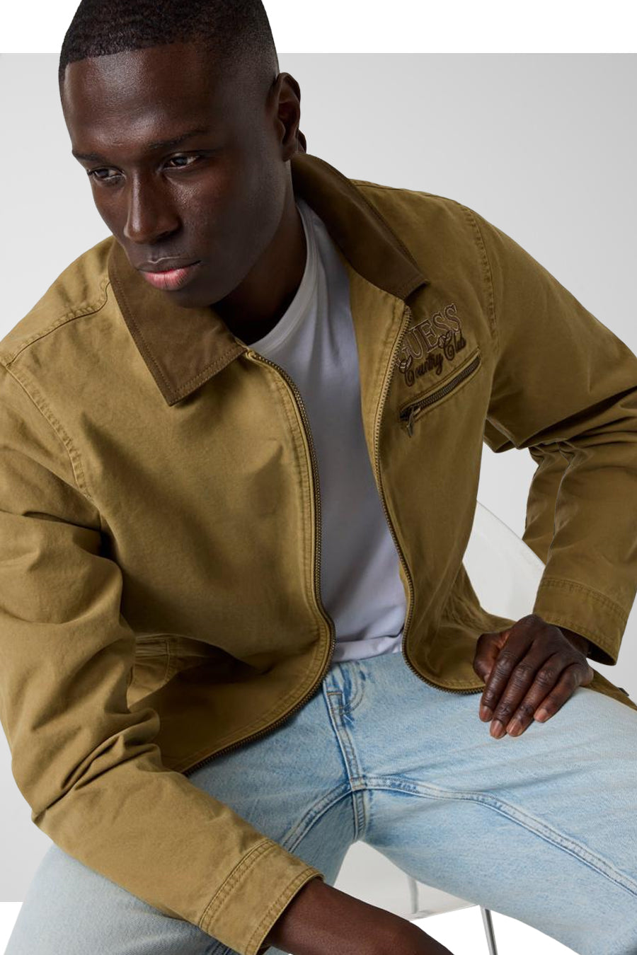 Bruine korte jas van Guess® met rits, borstzak en logo borduursel, gedragen met wit shirt en lichtblauwe jeans, zijprofiel.