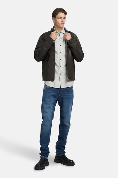 Jean bleu droit de REPLAY, associé à une chemise rayée et un manteau en cuir brun.