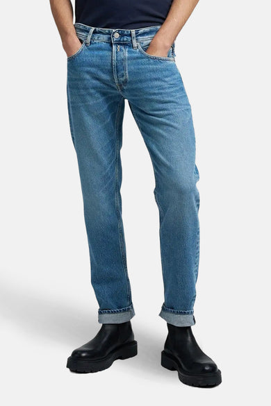 Jean droit en denim bleu moyen de Replay, avec des poches suréolées et des chaussures noires.