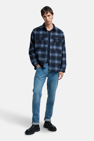 Jean bleu de REPLAY, porté avec un t-shirt bleu marine et une chemise rayée bleue et noire.